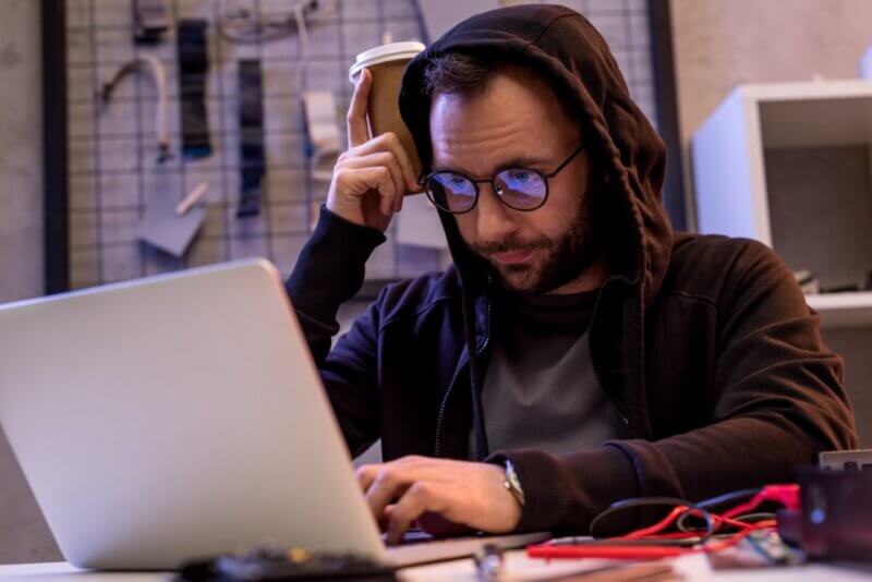Mann im Kapuzenpulli mit Laptop auf dem Tisch. So unscheinbar kann ein Hacker sein.